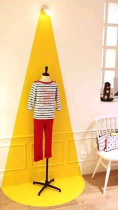 a mannequin is standing in front of a yellow triangle on a stand next to a white chair