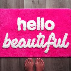 a pink rug with the words hello beautiful written in white on it and two pairs of bare feet standing next to it