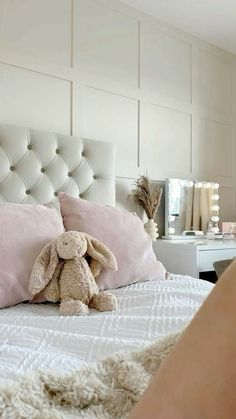 a stuffed animal sitting on top of a bed in a room with white walls and pink pillows