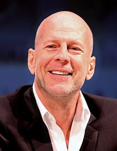 a bald man in a black jacket smiles at the camera