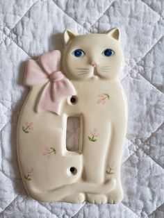 a ceramic light switch cover with a cat on it's side and a pink bow