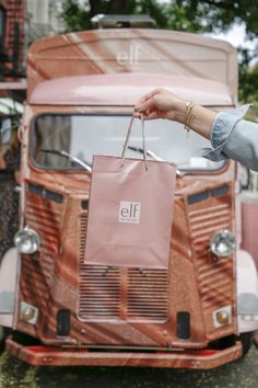 a hand holding an elf cosmetics bag in front of a pink vintage truck E.l.f. Cosmetics, Elf Cosmetics, Brand Promotion