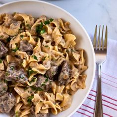 a white bowl filled with pasta covered in meatballs and parsley next to a fork