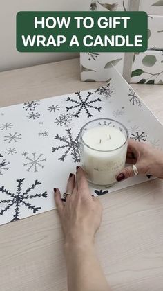 a person holding a candle on top of a table next to a paper snowflake