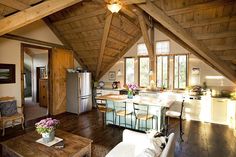 an open kitchen and living room area with wood beams on the ceiling, hardwood flooring