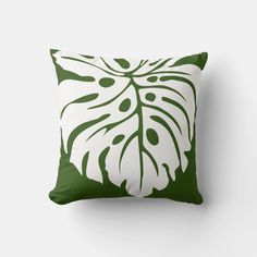 a green and white pillow with a large leaf design on the front, against a white wall