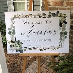 a welcome sign in front of a brick house with greenery on the frame and lettering that reads, welcome to agnes's baby shower