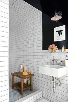 a white tiled bathroom with a sink and shelf on the left side of the room