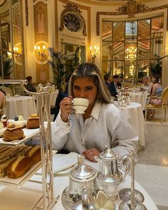 a woman sitting at a table drinking from a cup