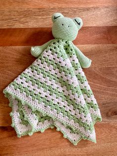 a crocheted green and white teddy bear laying on top of a wooden floor