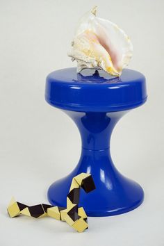 a sea shell on top of a blue pedestal next to black and white checkered ribbon