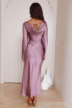 the back of a woman in a purple dress standing against a wall with her hands on her hips