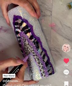 someone is decorating a purple and black pillow with glitters on it, while another person holds a cell phone in front of them