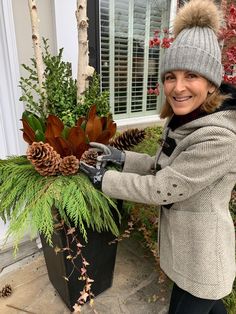 a woman in winter clothing placing pine cones on a planter