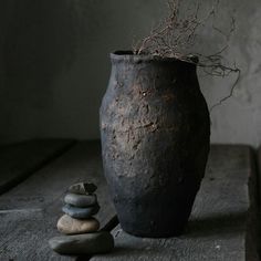 a black vase sitting on top of a wooden table next to rocks and a plant