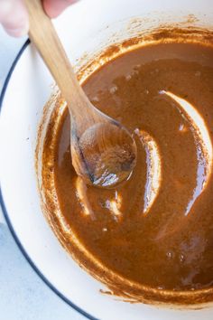 a wooden spoon in a white bowl filled with brown sauce