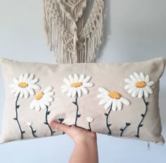 a hand holding a pillow with daisies embroidered on it