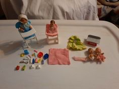 two dolls are sitting in chairs and other toys on a tray next to a bed