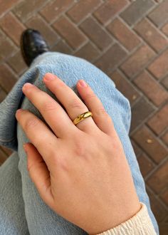 a person's hand with a gold ring on their left wrist, sitting next to a brick wall