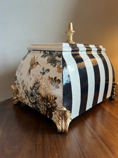 a black and white striped box sitting on top of a wooden table next to a lamp