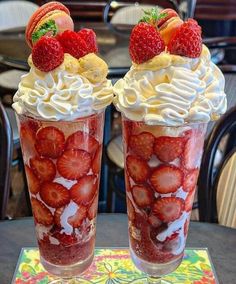 two cups filled with whipped cream and strawberries on top of a table next to each other