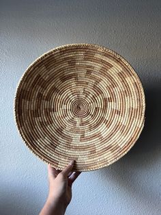 a person holding up a woven basket on the wall with their hand in front of it