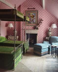 a bedroom with pink wallpaper and green bedspread, two blue chairs and a painting on the wall