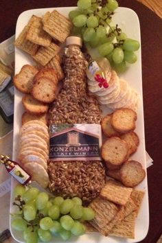 a wine bottle surrounded by crackers, grapes and other snacks on a plate with corkscrews