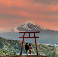 two people standing in front of a red chair with a mountain in the back ground