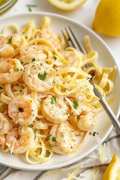 a white plate topped with pasta and shrimp next to lemon wedges on a table