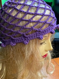 a mannequin head wearing a purple crochet hat on top of a wooden table