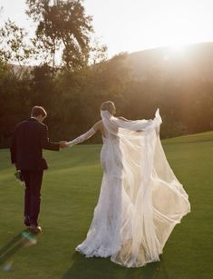 a bride and groom holding hands while walking through the grass