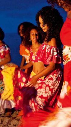 several women in colorful dresses dancing on the beach at night with blue sky and water behind them