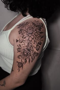 a woman's shoulder with flowers and leaves tattooed on her left arm, in black and white