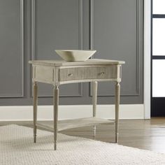 a white table with a bowl on it in front of a gray wall and rug