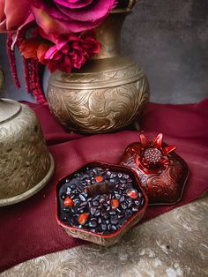 two decorative dishes sit on a red table cloth next to a gold vase with flowers in it