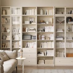 a living room filled with lots of white furniture and bookshelves full of books