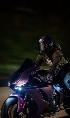 a man riding on the back of a purple motorcycle at night with headlights shining down