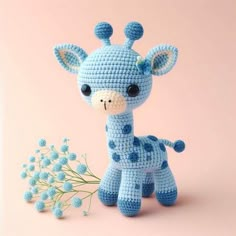 a blue crocheted giraffe next to some baby flowers on a pink background