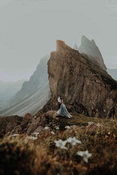 a woman standing on top of a mountain next to a tall rock covered in snow