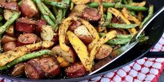 a pan filled with potatoes and asparagus on top of a red table cloth