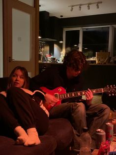 two people sitting on a couch playing guitars