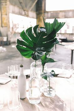 the table is set with empty wine glasses, bottles and greenery in glass vases