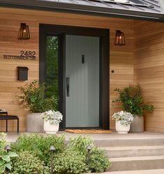 two potted plants sit on the front steps of a house with a gray door