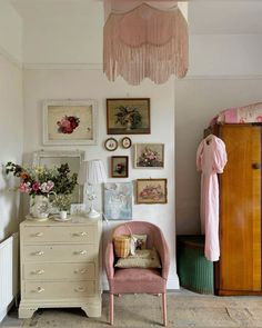 a pink chair sitting next to a dresser in a room with pictures on the wall