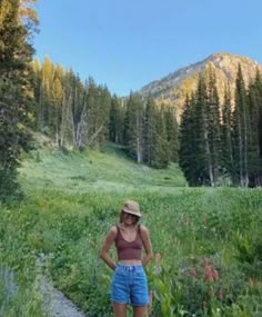 a woman standing in the middle of a field with mountains in the backgroud