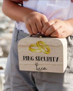 a person holding a wooden box with two wedding rings on it that says ring security