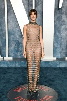 a woman standing on top of a blue carpet wearing a dress with chains around it