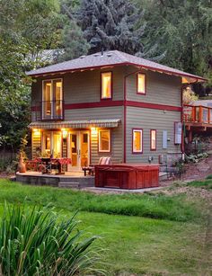 a house with lights on in the front yard and trees behind it, surrounded by lush green grass