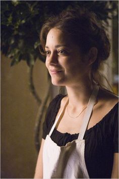 a woman wearing an apron and smiling at the camera with a potted plant in the background